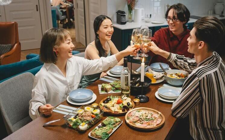 quatre amis partagent un dîner autour d'une table, ils trinquent et rigolent