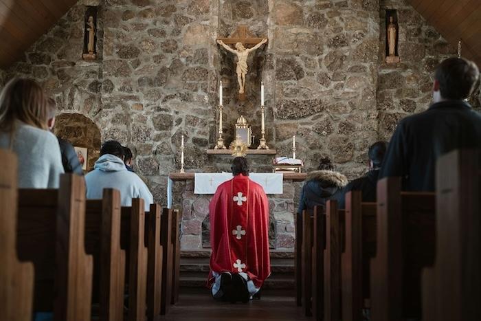 un pretre de dos et des croyants en train de prier face à un crucifix dans une église