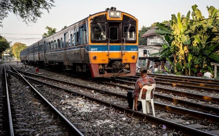 Un homme assis sur la voie ferree pres d'un train a Bangkok