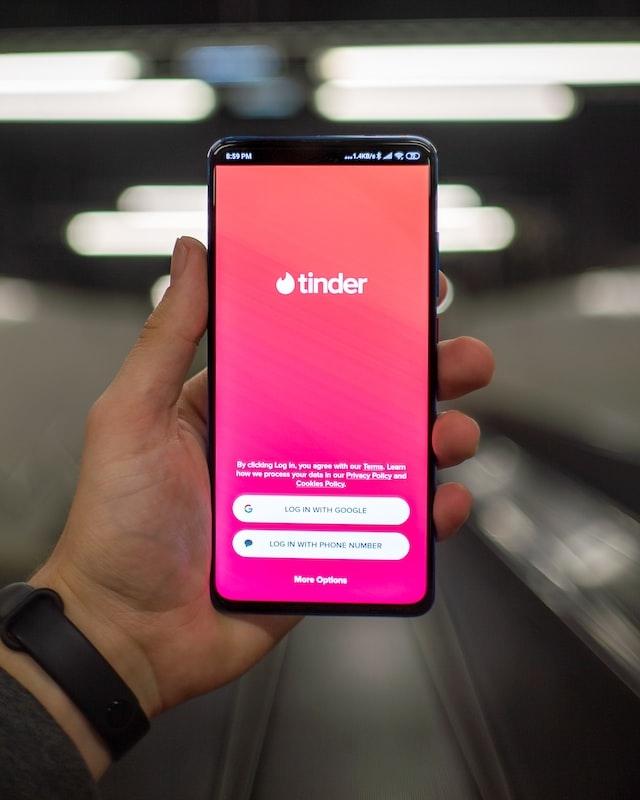 une main qui tient un portable avec un ecran tinder rose