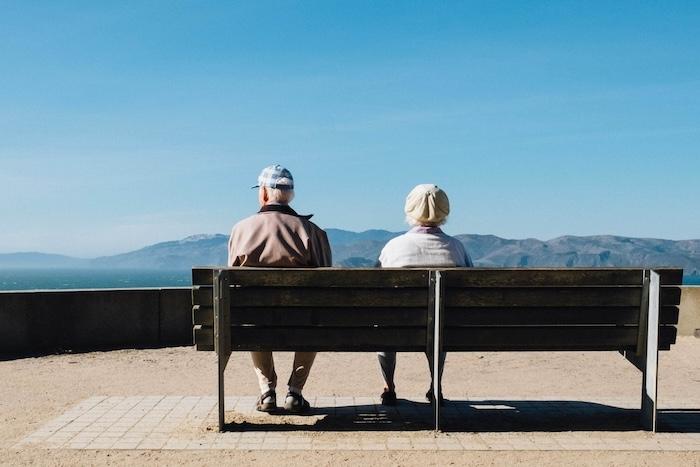 deux personnes agées sur un banc face à un paysage de mer et de montagnes