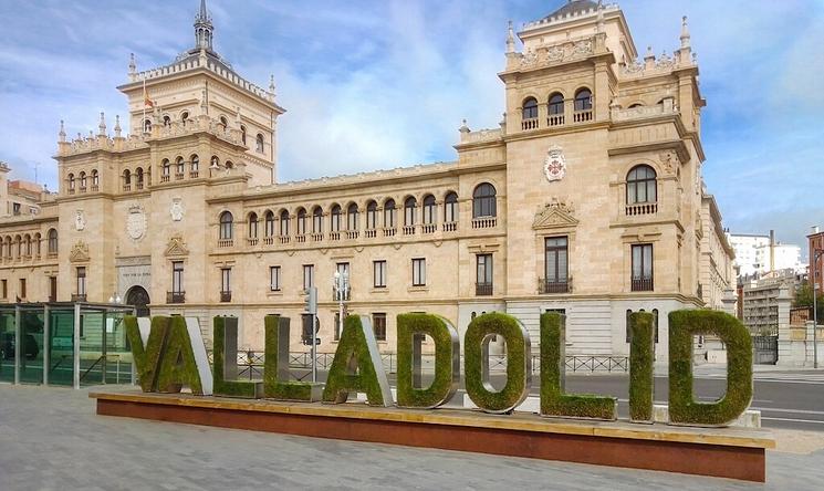 Une grande enseigne verte avec l'inscription "Valladolid" devant un majestueux bâtiment historique en pierre