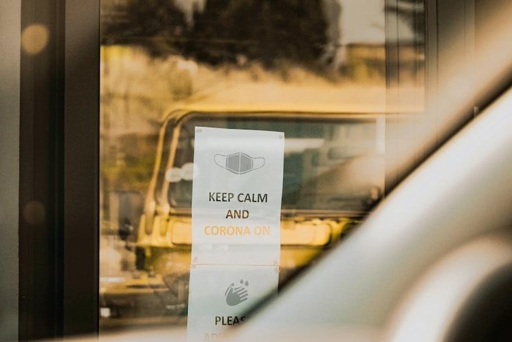 Une vitre avec une affiche où il est écrit "Keep calm and Corona on"