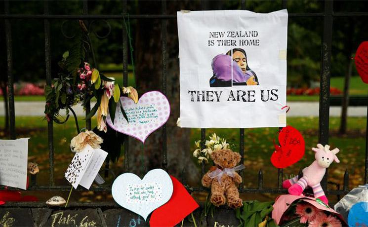 Grillage avec de nombreux bouquets de fleur et une affiche "they are us"