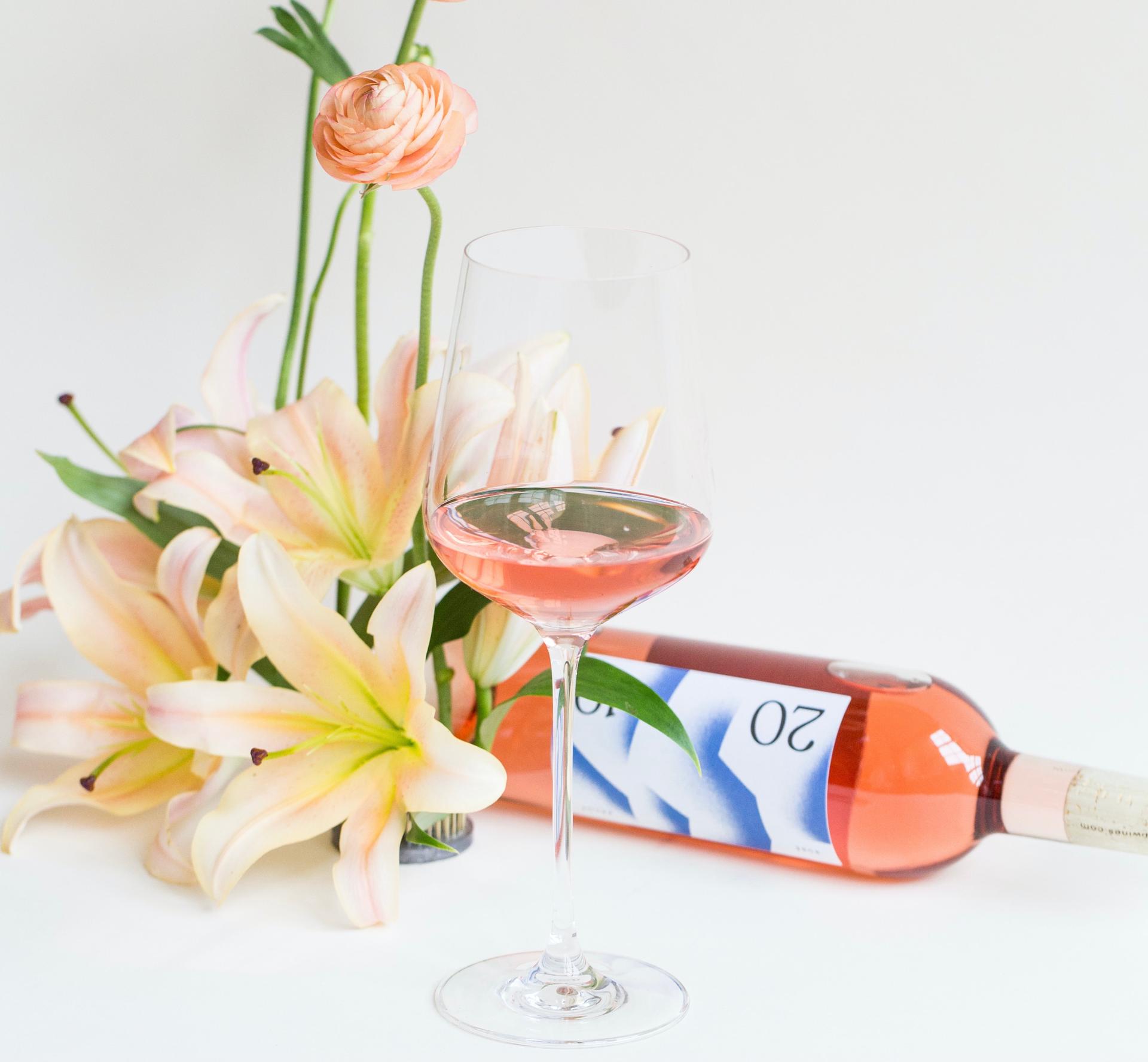 Une bouteille de rosé couleur pastel trônent aux côtés de fleurs qui lui sont assorties