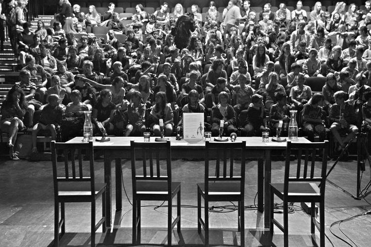 Une table de lecture installée sur une scène devant une salle pleine.