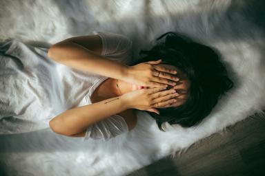 Une femme couchée dans son lit qui se tient la tête entre les deux mains