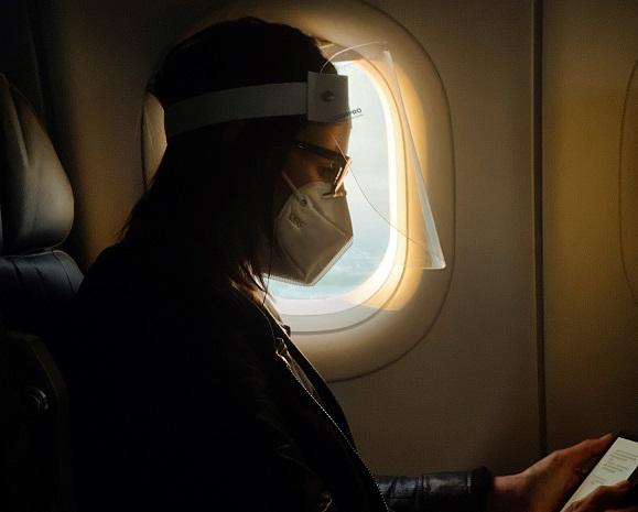 une personne avec masque regarde son telephone dans un avion