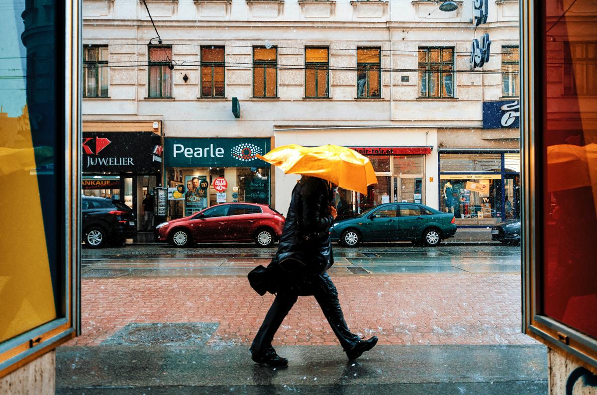 Un homme avec un parapluie jaune marchant contre le vent.