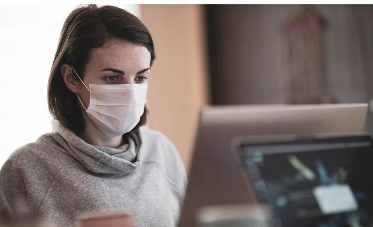 une femme porte un masque covid devant son ordinateur
