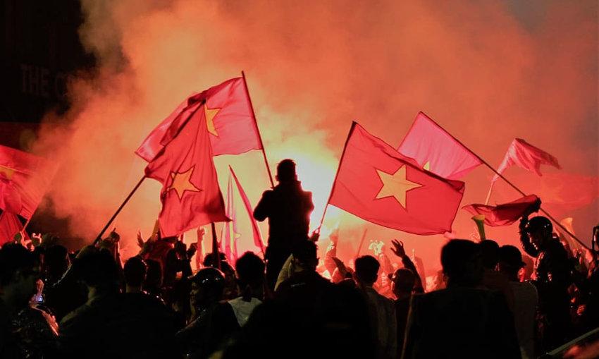 une foule la nuit brandissant des drapeaux vietnamiens rouges et jaunes