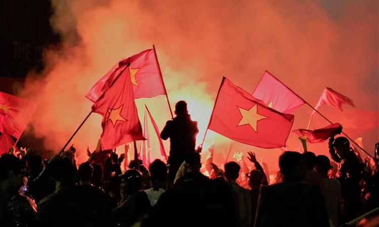 une foule la nuit brandissant des drapeaux vietnamiens rouges et jaunes