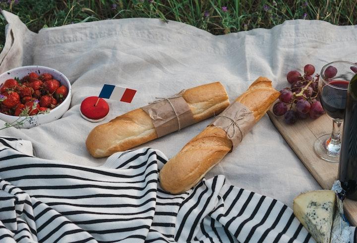 Une baguette, un verre de vin, des fruits, du fromage et un drapeau français