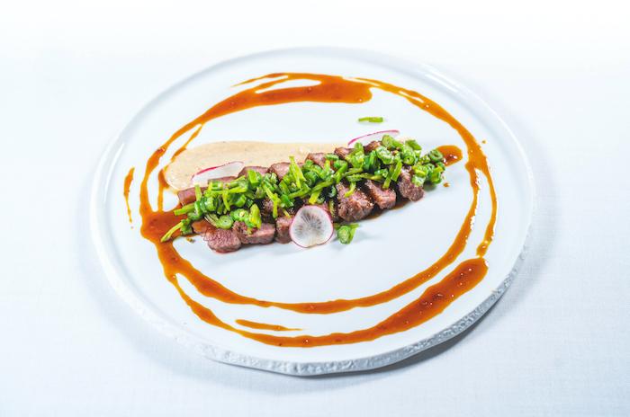 Des fines tranches de viande avec des légumes verts et de la sauce dans une assiette blanche