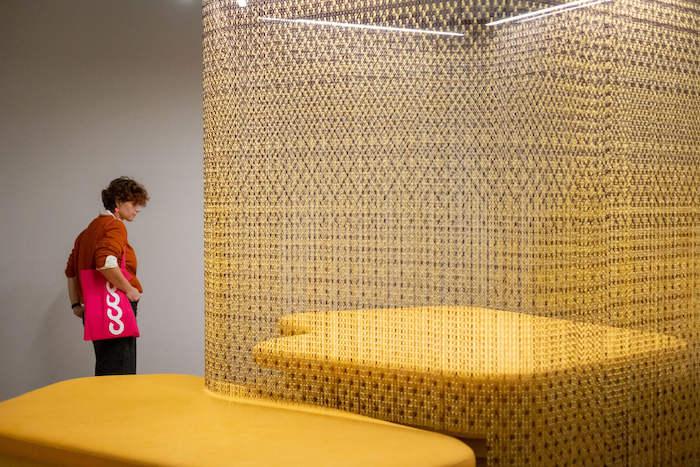 une personne avec un sac violet en train de regarder des canapés jaunes au Centre del Carme dans l'exposition Escenarios de un Futuro Cercano