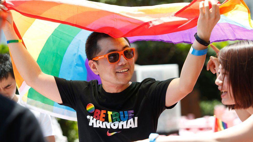 un homme lgbt en chine avec un drapeau arc en ciel et tee shirt shangha pride