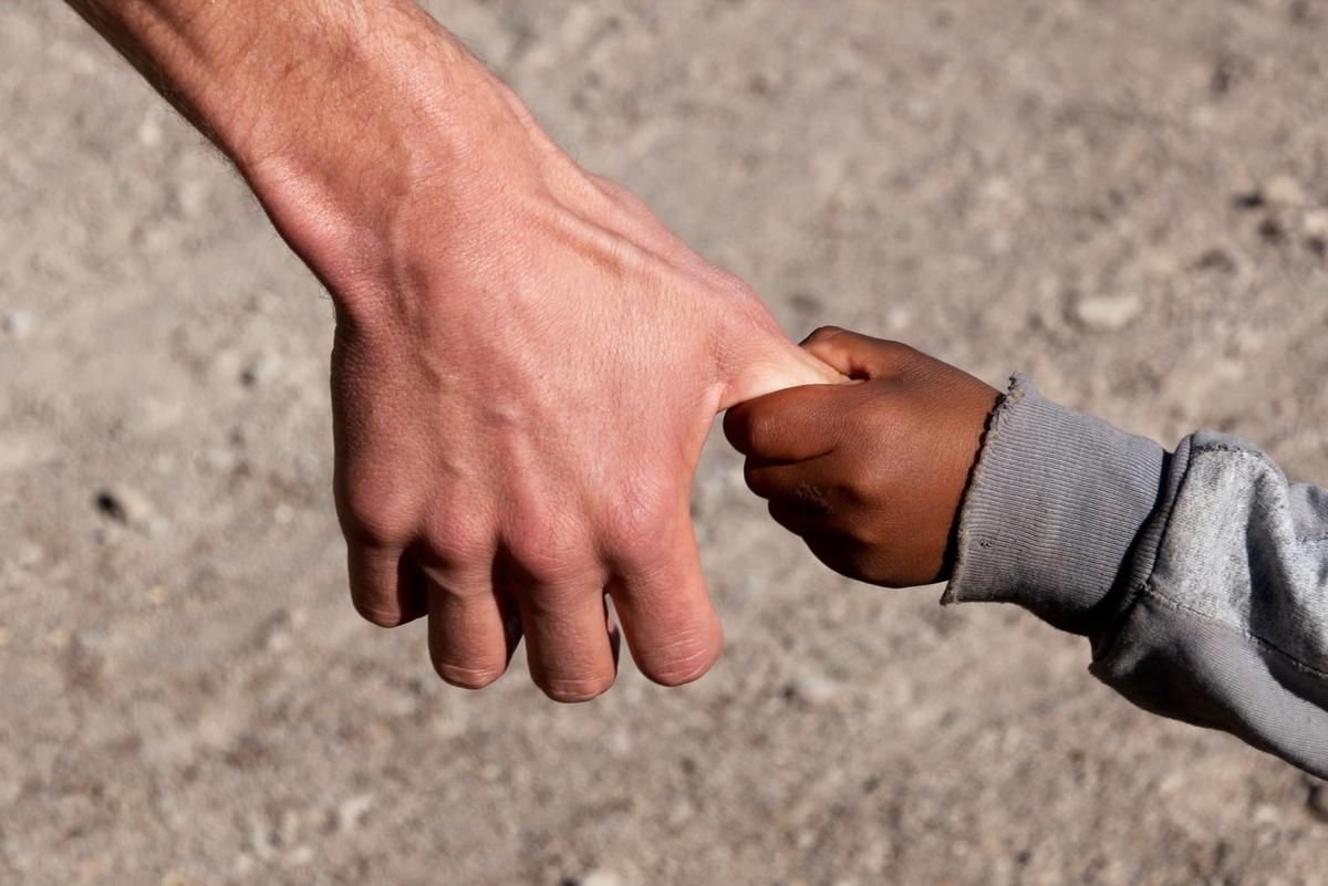 Pourquoi l'adoption internationale est en baisse ? Un enfant adopté tente de tenir la main d'un adulte adoptant