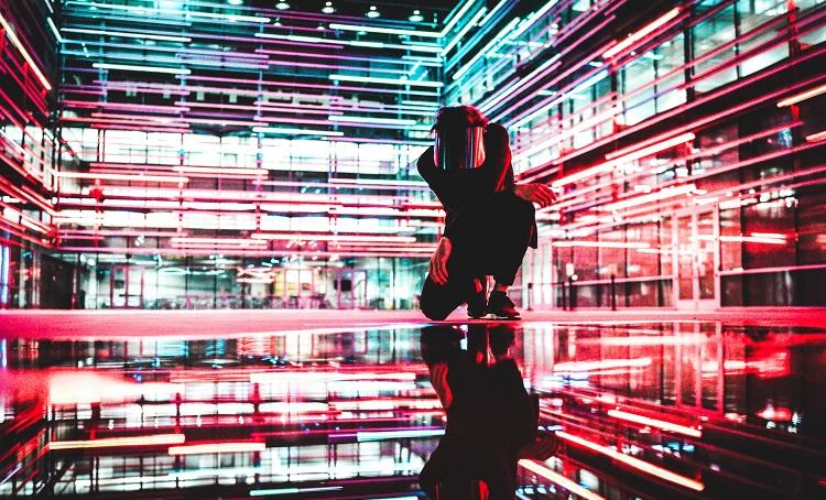 un homme accroupi au milieu de faisceux lumineux rouges - drew-dizzy-graham--unsplash