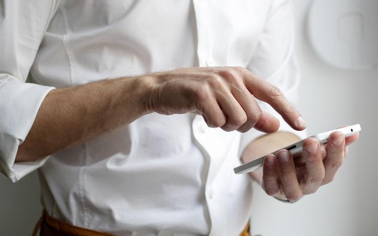 un homme en chemise blanche touche du doigt l'écran de son téléphone portable - nordwood-themes-unsplash_0