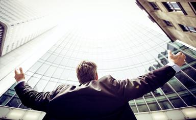 un homme lève les bras vers un gratte ciel avec succès - razvan-chisu-unsplash