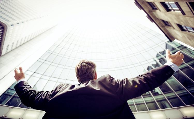 un homme lève les bras vers un gratte ciel avec succès - razvan-chisu-unsplash
