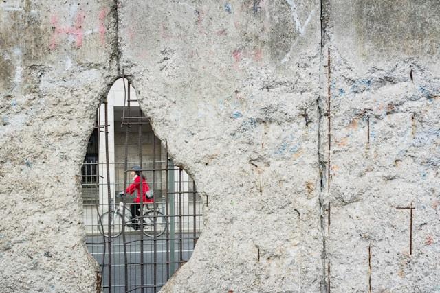 Mur de Berlin troué, avec une cycliste passant derrière