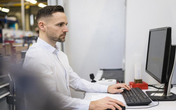 businessman-using-computer-at-desk-in-a-factory-2023-11-27-05-09-15-utc