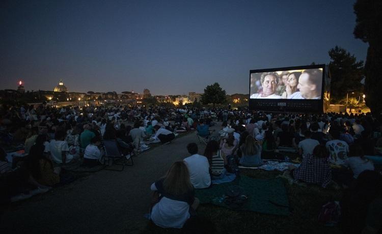 des gens regardent un écran de cinéma en plein air de nuit