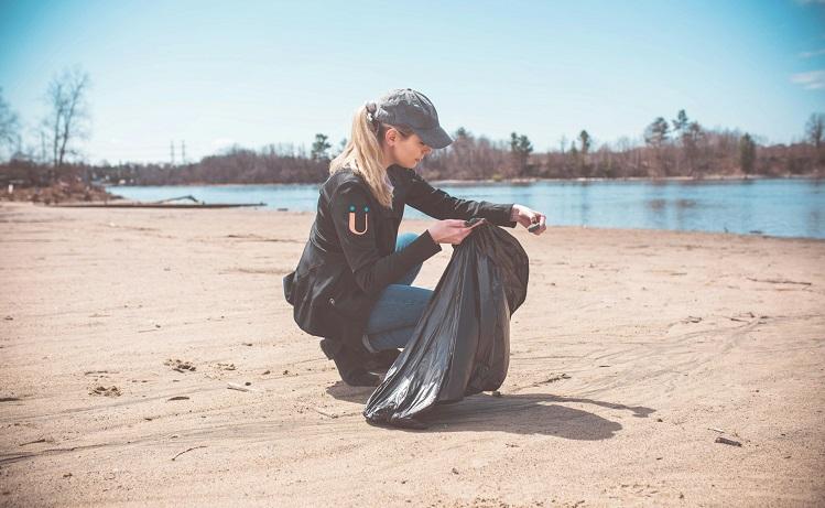 une femme avec une casquette nettoie une plage avec un sac poubelle noir