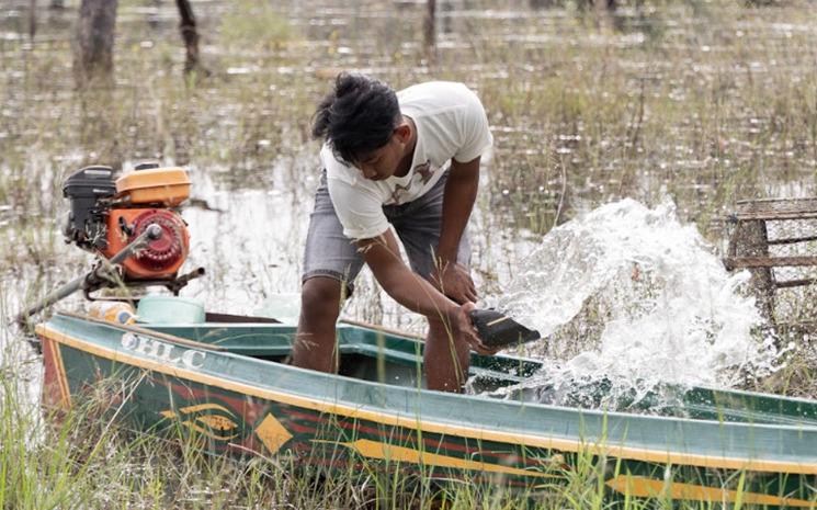 Un villageois retire l'eau de son bateau alors qu'il se prépare à visiter leur village inondé.