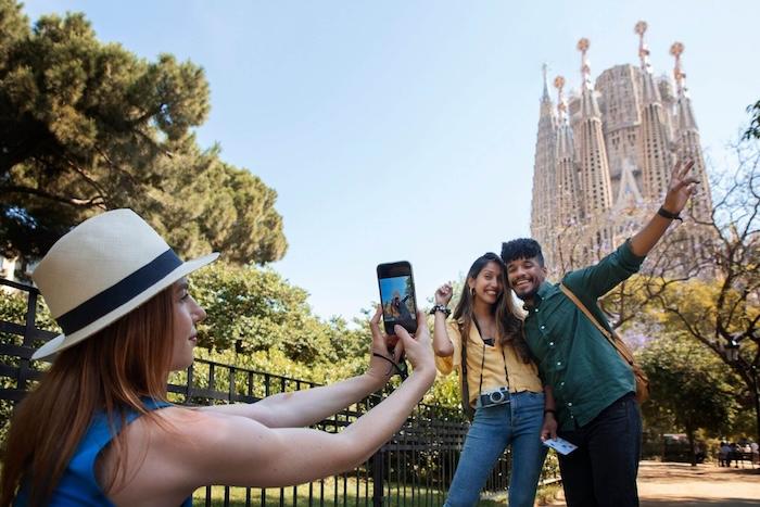 vue latérale d'une femme en train de prendre une photo de touristes devant la sagrada famila à Barcelone