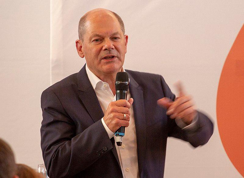 Olaf Schloz lors d'une conférence avec un micro à la main