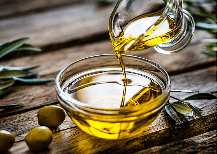 Versement d'huile d'olive extra-vierge dans un bol en verre, entourée d'olives et de feuilles, représentant les huiles turques du classement EVOOLEUM 2025.