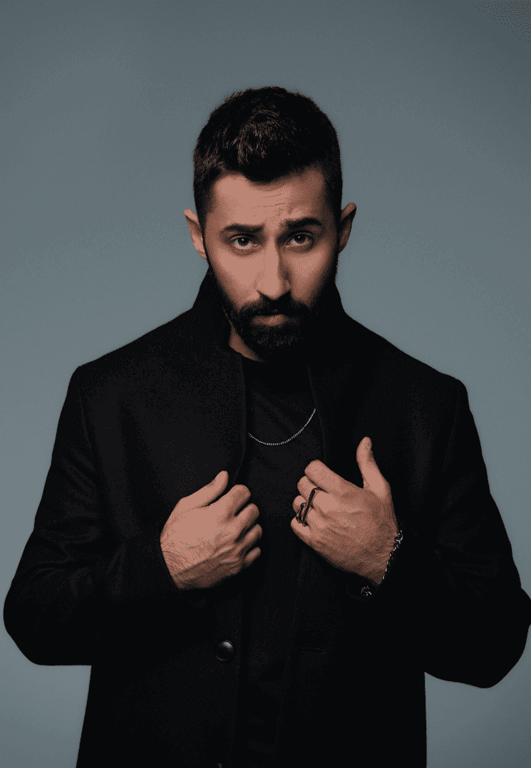 Portrait de Sancak, artiste emblématique du RnB turc, vêtu d’un manteau noir élégant, promouvant son concert romantique et émouvant à Izmir en janvier 2025.