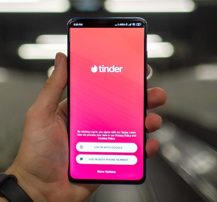 main tenant un smartphone android avec l'app rencontres Tinder ouverte sur l'écran