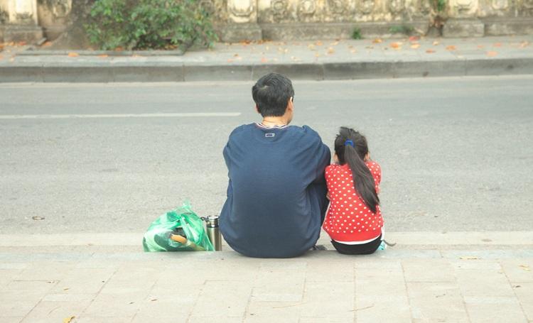 un homme et une peitte fille assis au bord d'un trottoir