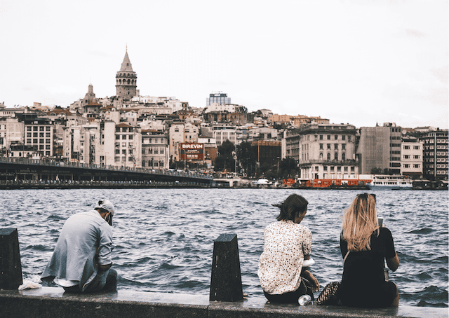Trois jeunes assis au bord du Bosphore à Istanbul, absorbés par leurs téléphones, illustrant la FOMO et l’isolement numérique.