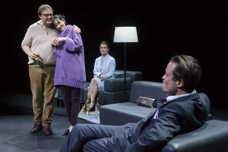 Un homme de dos assis dans un fauteuil fait face à un homme et une femme enlacés et debout. Derrière eux, une femme est assiste et les regarde