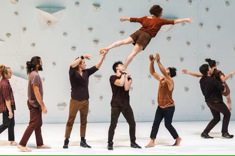 Huit danseurs font des acrobaties devant un mur d'escalade