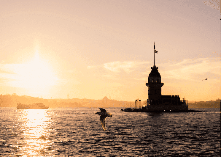 Coucher de soleil sur la tour de Léandre à Istanbul, avec une mouette en vol et le Bosphore paisible en arrière-plan.