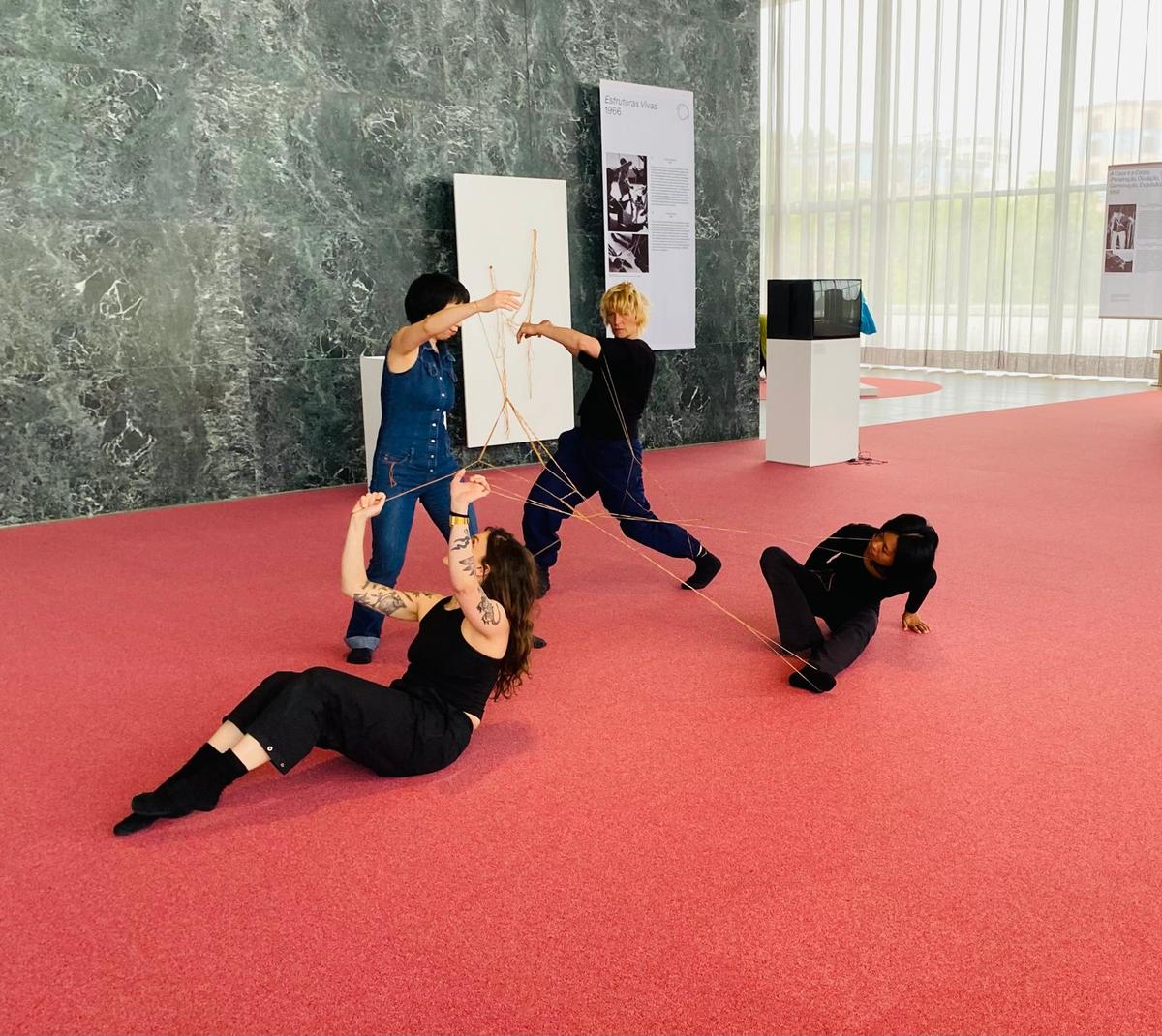 Quatres femmes bougent au sein de l'exposition en étant entrelacées par un élastique