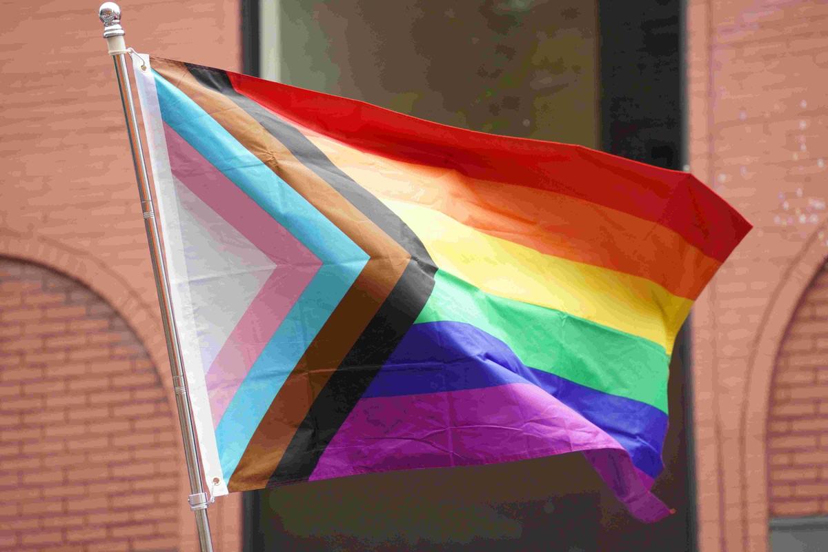 Le drapeau LGBTQIA+ flotte devant un mur de briques rouges