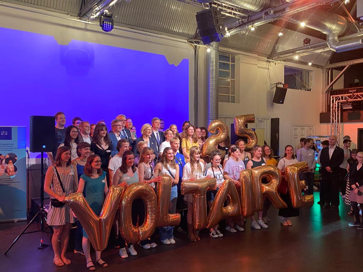 Des participants du programme Voltaire rassemblés tiennent des ballons qui écrivent "25 Voltaire"