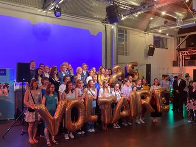 Des participants du programme Voltaire rassemblés tiennent des ballons qui écrivent "25 Voltaire"