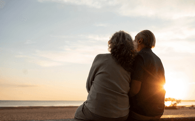Un couple s'enlace devant un coucher de soleil sur une plage.
