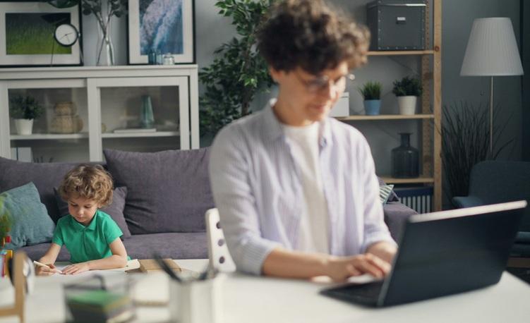 Une femme assise devant son ordinateur avec son enfant derrière