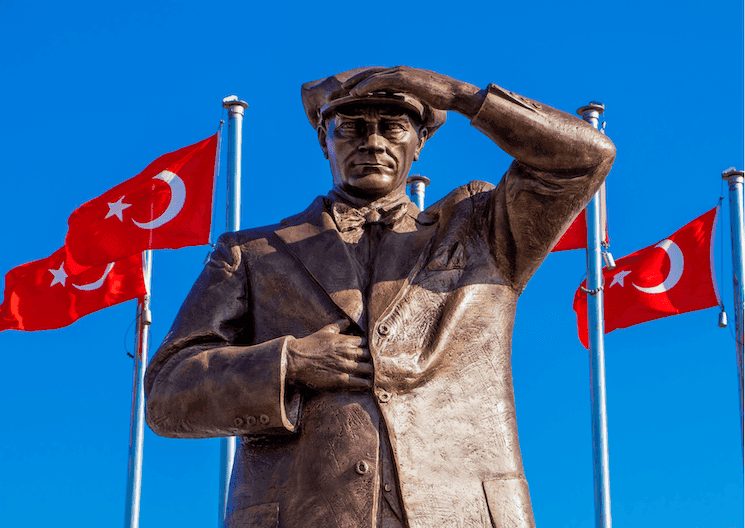 Statue de Mustafa Kemal Atatürk à Marmaris, devant des drapeaux turcs, sous un ciel bleu.