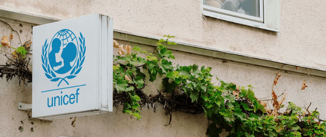 UNICEF appel aux dons affiche blanc bleu sur mur beige avec végétation