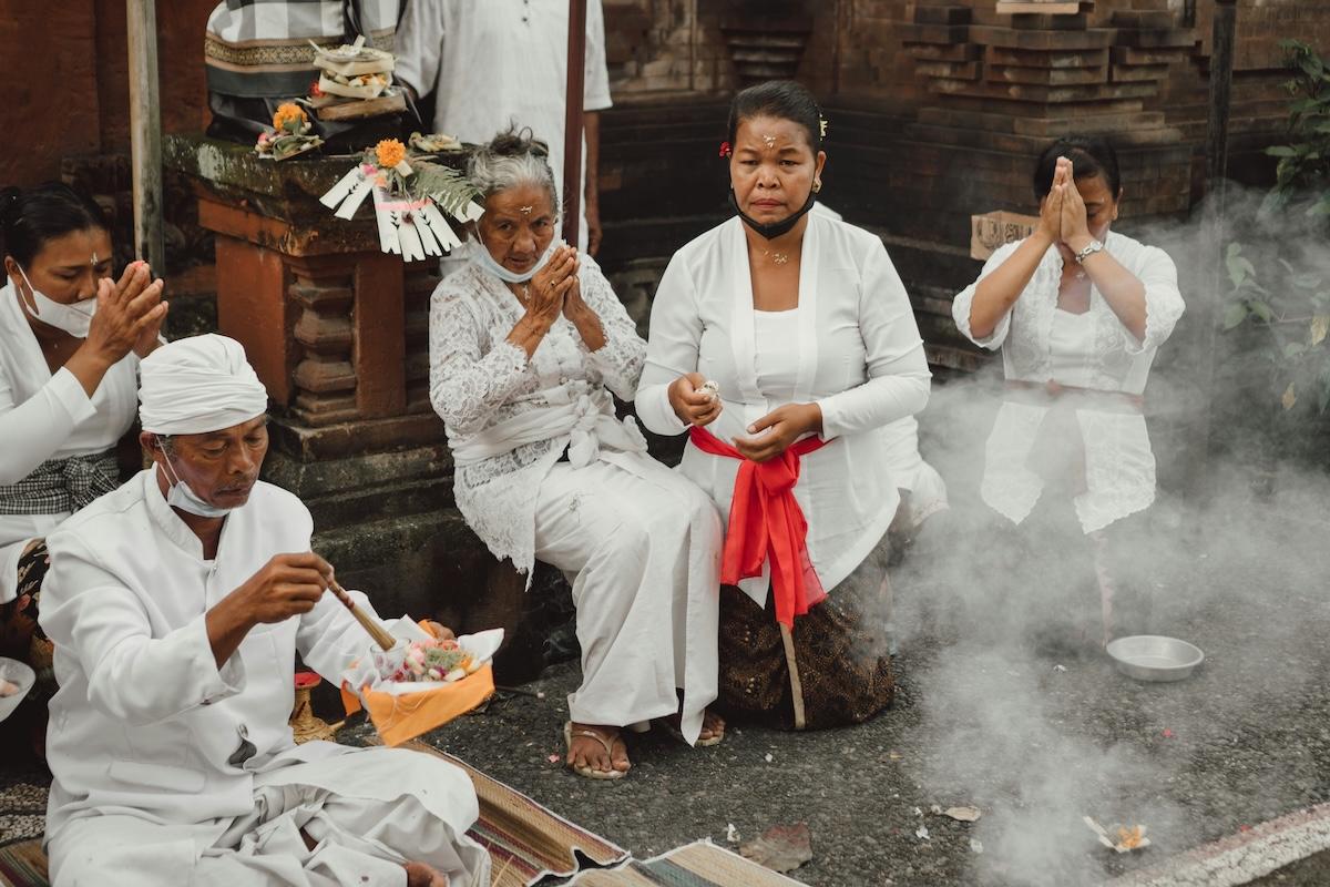 quatre balinais habillés en blanc qui prient dans un temple