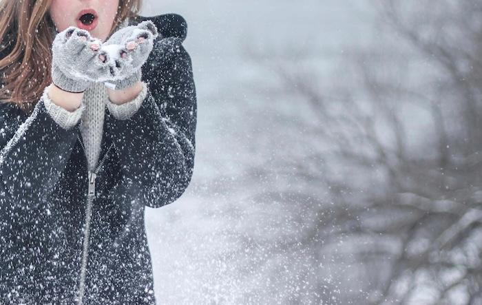 femme avec veste a capuche zippee noire soufflant sur de la neige